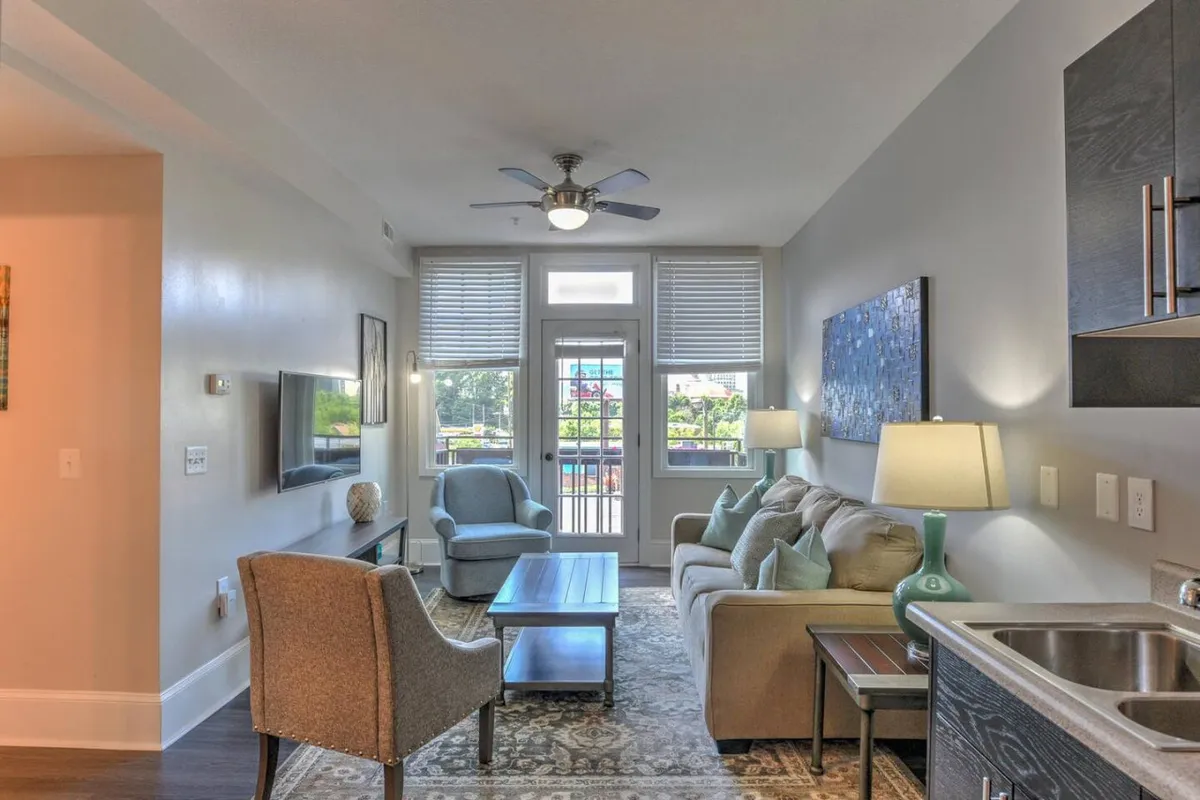 This image features a bright and inviting living room with a comfortable sofa, a well-styled coffee table, modern artwork on the wall, and expansive balcony doors that let in abundant natural light. The room is arranged to encourage both relaxation and conversation, while the balcony doors hint at seamless indoor-outdoor living.
