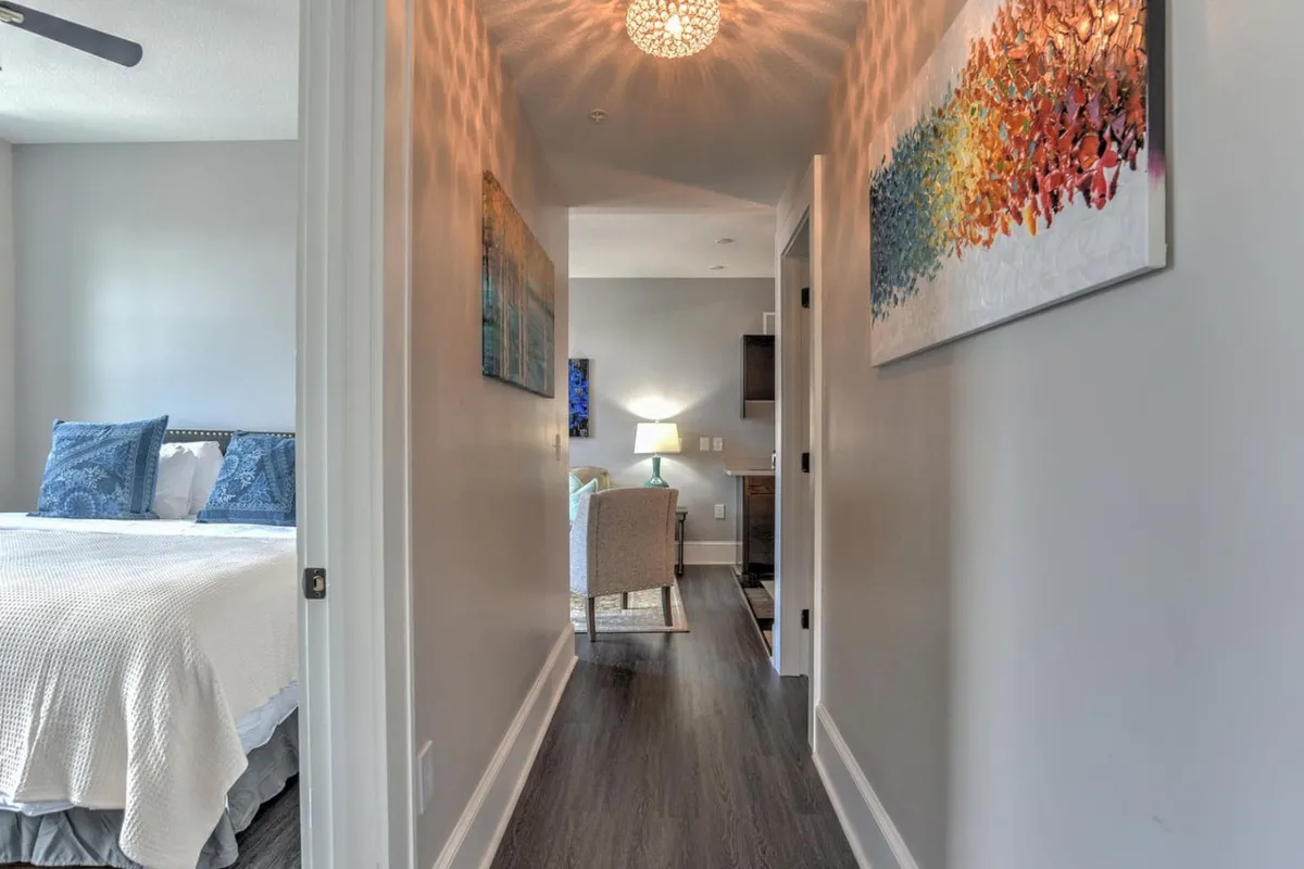 This image captures a soft-lit hallway adjacent to a bedroom, with warm light spilling onto detailed molding, artwork on the walls, and inviting decor. The visible hallway emphasizes the transition space and hints at the historic character of the building.