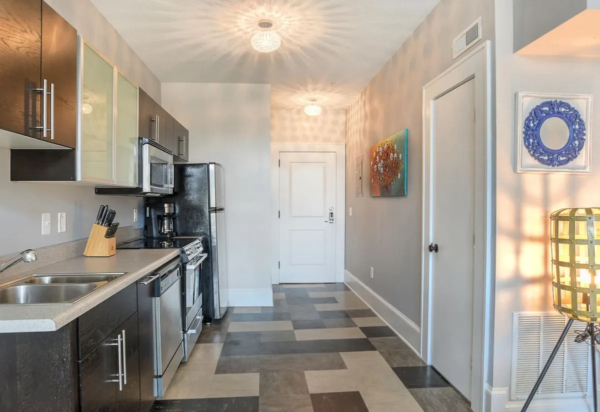 A partial view that transitions into the open dining area, showcasing modern kitchen appliances, stylish light fixtures, decorative wall art, and rich flooring. The open-plan layout allows for easy flow between cooking, dining, and social moments, ideal for hosting and casual dining.
