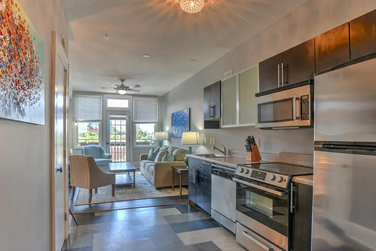 A wide view of an open-plan living area that includes a glimpse of the hallway, kitchen, and dining space. Artworks and creative touches are visible along the corridor, reinforcing the sense of character and continuity.