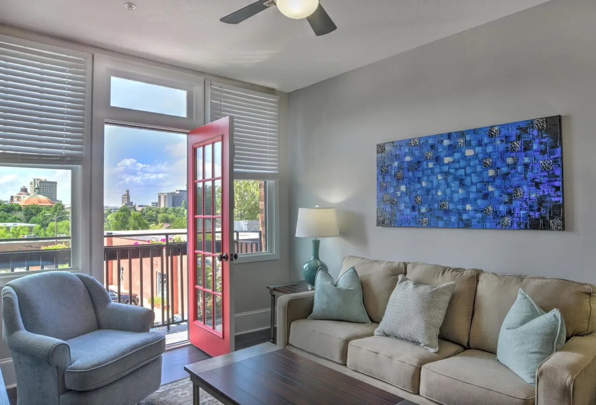 The image centers on a striking red entry door set within an interior space, complemented by abstract art and a cozy sofa. The space exudes a cheerful, welcoming mood and highlights unique architectural details and vibrant decor.