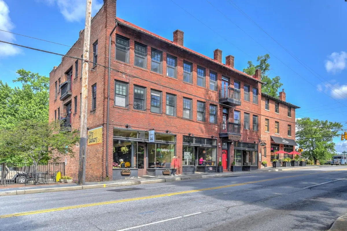 This image captures a vibrant streetscape featuring historic brick architecture, distinctive storefronts with large windows, and balconies adorned with plants. The scene suggests a lively area where people shop at local boutiques and dine at nearby cafes, with a sense of community and charm.
